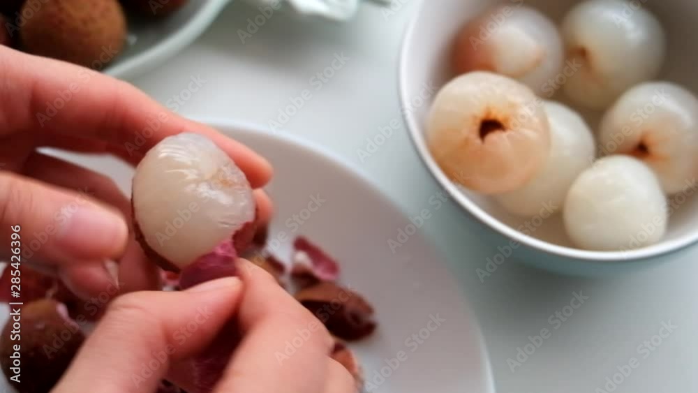 Peeling juicy and plump lychee and depositing it into a small ceramic round bowl, while discarding the peels in a white plate. Peeling juicy and plump lychee and depositing it into a small ceramic round bowl, while discarding the peels in a white plate.