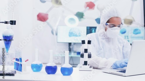 Female scientist working in a modern laboratory with reagent in test tubes with blue liquid and adjusting microscope. Scientist using laptop for research. photo