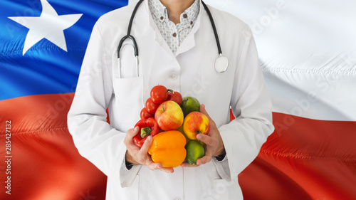 Doctor is holding fruits and vegetables in hands with Chile flag background. National healthcare concept, medical theme.