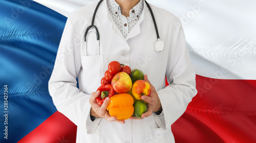 Doctor is holding fruits and vegetables in hands with Czech Republic flag background. National healthcare concept, medical theme.