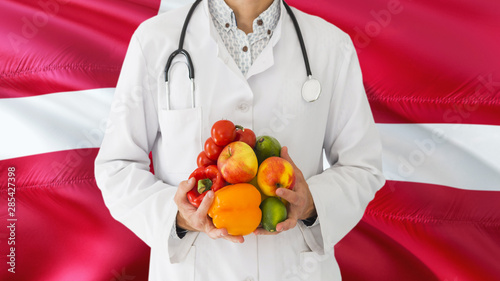 Doctor is holding fruits and vegetables in hands with Denmark flag background. National healthcare concept, medical theme.