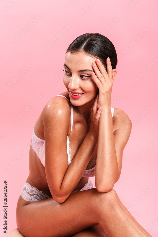 Obraz premium Photo of joyful young woman wearing white sexual lace lingerie smiling and sitting at camera