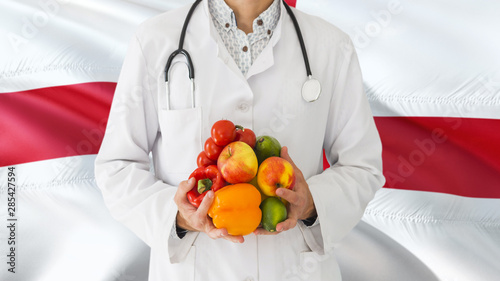 Doctor is holding fruits and vegetables in hands with England flag background. National healthcare concept, medical theme.