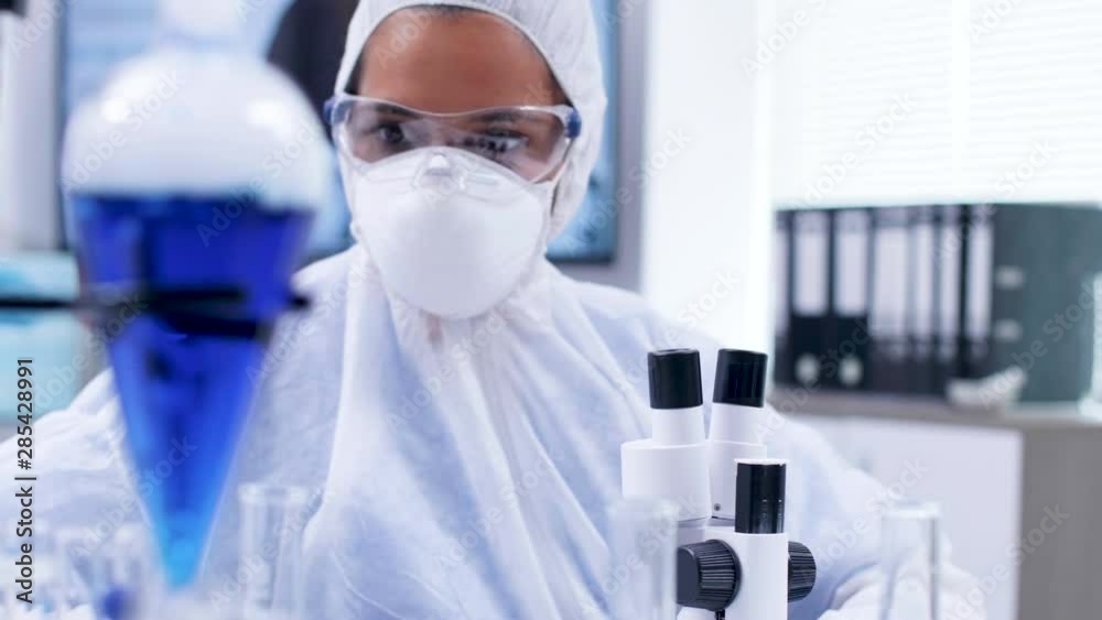 Female scientist in coverall equipment holding and looking at est tube with blue liquid. Chemical scientist in modern laboratory.
