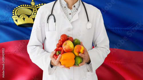 Doctor is holding fruits and vegetables in hands with Liechtenstein flag background. National healthcare concept, medical theme.