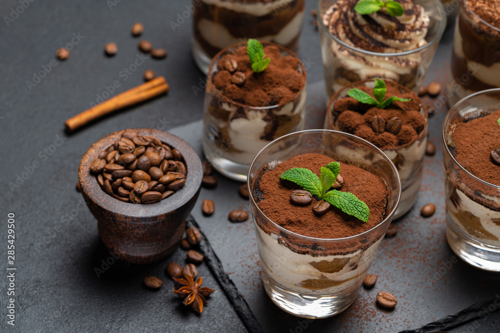 Group of portions of Classic tiramisu dessert in a glass cup on stone board on concrete background Group of portions of Classic tiramisu dessert in a glass cup on stone board on concrete background