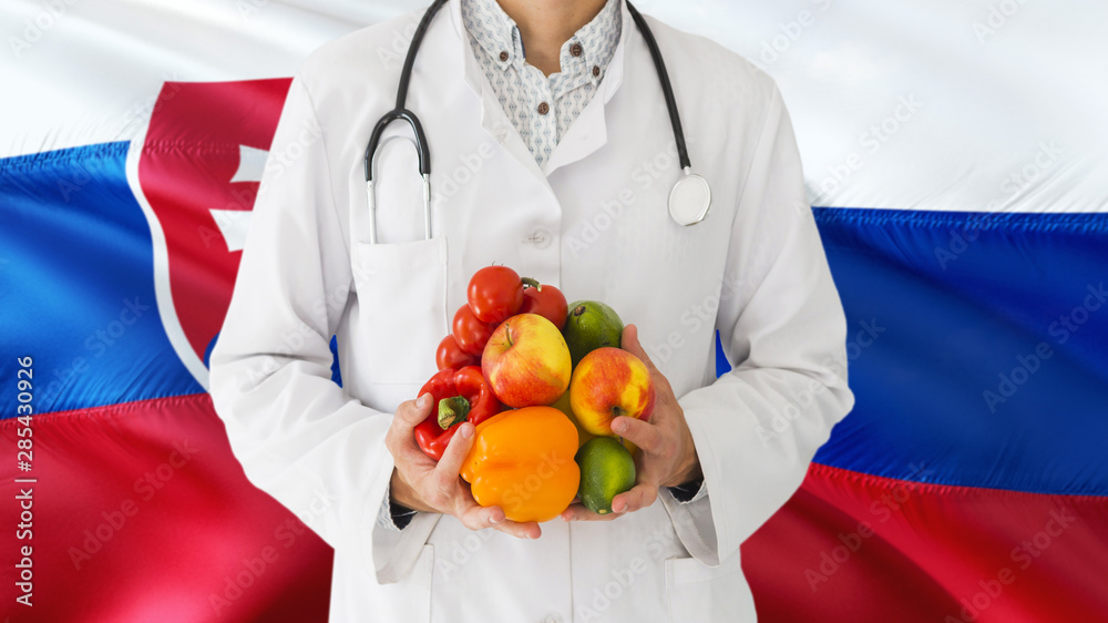 Doctor is holding fruits and vegetables in hands with Slovakia flag background. National healthcare concept, medical theme. Doctor is holding fruits and vegetables in hands with Slovakia flag background. National healthcare concept, medical theme.