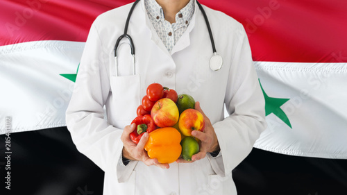 Doctor is holding fruits and vegetables in hands with Syria flag background. National healthcare concept, medical theme.