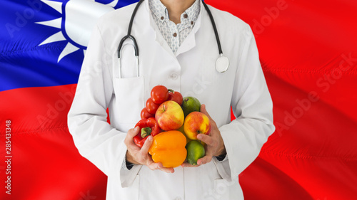 Doctor is holding fruits and vegetables in hands with Taiwan flag background. National healthcare concept, medical theme.