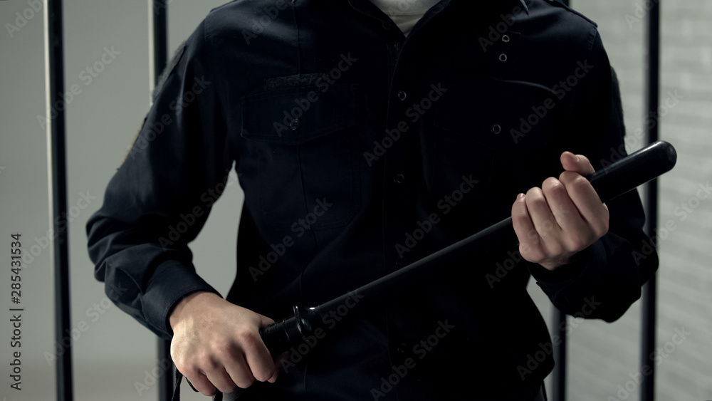 Prison security guard standing near cell with truncheon, strict regime, violence Prison security guard standing near cell with truncheon, strict regime, violence