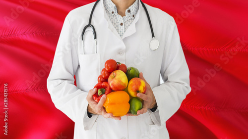 Doctor is holding fruits and vegetables in hands with Tunisia flag background. National healthcare concept, medical theme.