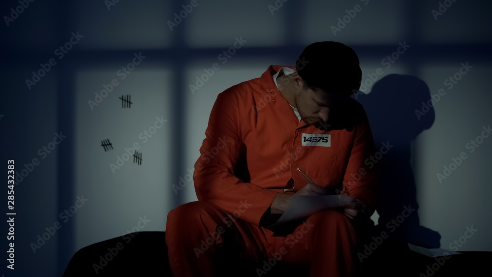 Caucasian male prisoner writing letter, missing family, composing mercy petition