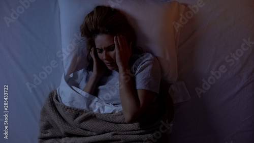 Young lady holding head in bed, suffering headache after awakening at night