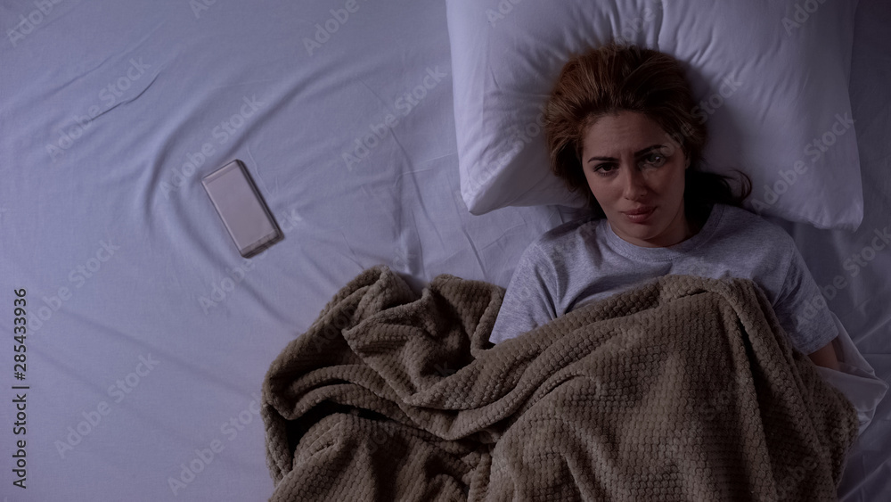 Sad lady lying in bed, phone beside, waiting for call from husband, break up