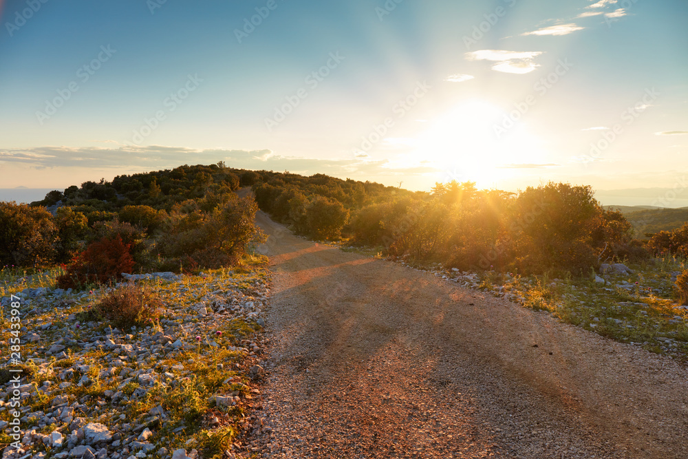 The sun sets over a country road. Mediterranean vegetation