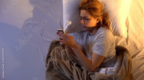 Sleepy girl turning off alarm clock and checking to-do list for today on phone
