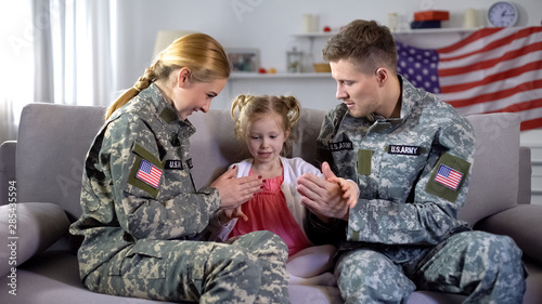 Cheerful US military couple playing pat-a-cake with little daughter at home