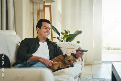 Photography Relaxed man lying with his dog on sofa watching tv in living roo