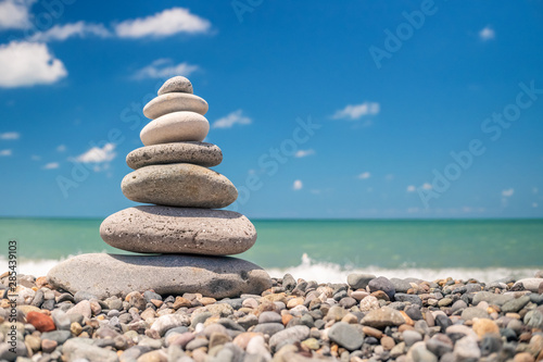 pyramid of sea pebbles on the beach against the backdrop of the sea wave in sunny day. concept of balance harmony and meditation. copy space