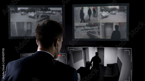 Fotografie, Tablou Security guard in earphones watching robbery attempt on surveillance cameras