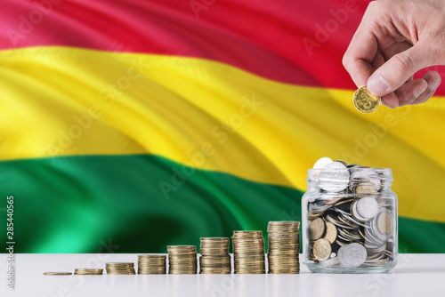 Business man holding coins putting in glass, Bolivia flag waving in the background. Finance and business concept. Saving money. photo