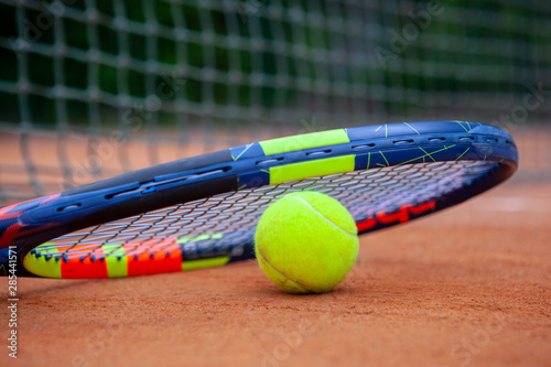 Yellow tennis ball and racket lie on the clay court. © Dmytro Panchenko