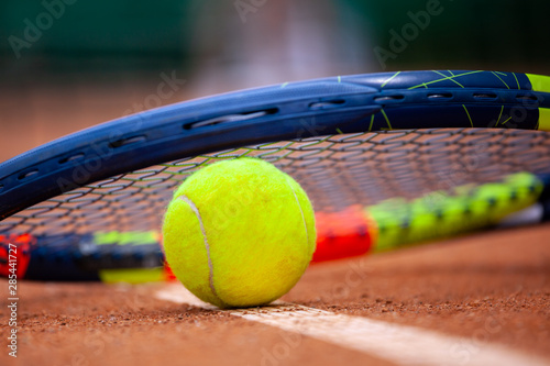 Yellow tennis ball and racket lie on the clay court. © Dmytro Panchenko