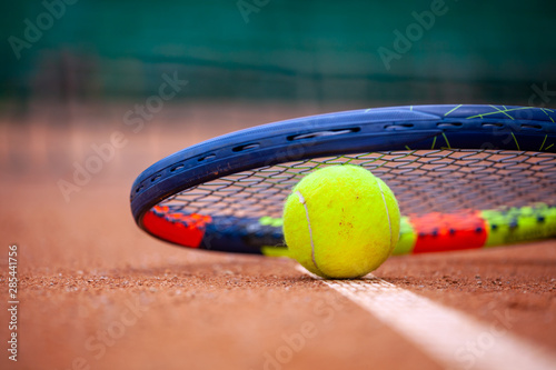 Yellow tennis ball and racket lie on the clay court. © Dmytro Panchenko