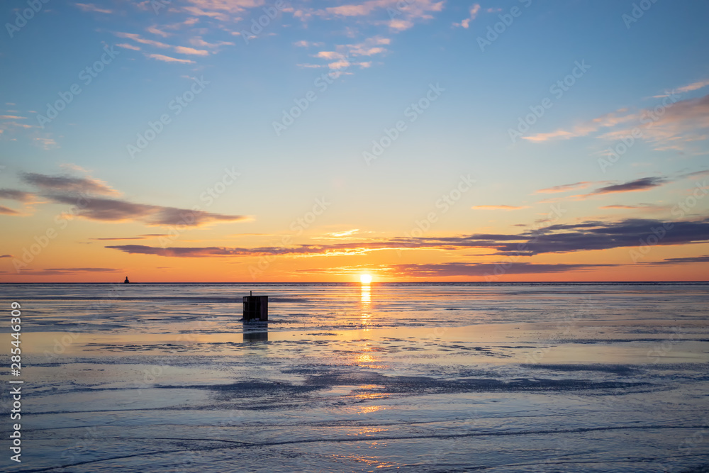 The sun setting over a frozen harbor and an ice fishing shack in rural Prince Edward Island, Canada. Lighthouse on the horizon.......