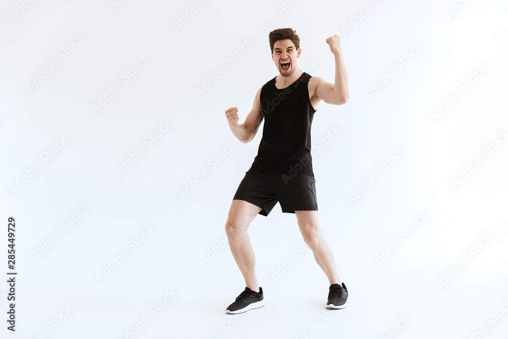 Strong young sports man running isolated over white wall background make winner gesture.