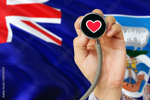 Doctor holding stethoscope with red love heart. National Falkland Islands flag background. Healthcare system concept, medical theme.