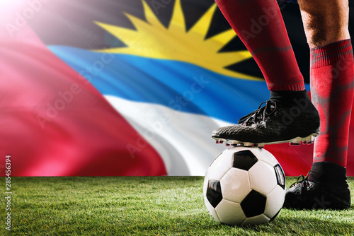 Close up legs of Antigua and Barbuda football team player in red socks, shoes on soccer ball at the free kick or penalty spot playing on grass.