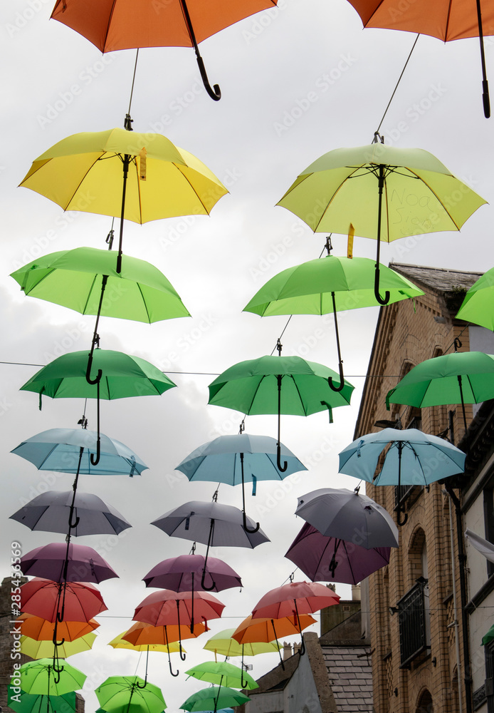 Wales, the historic town city of Caernarfon.  Inside the walled town, jolly, coloured umbrellas are placed above a narrow, old shopping street, giving the surroundings a touch of humour.
