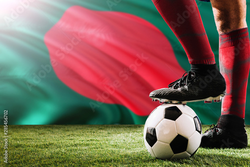 Close up legs of Bangladesh football team player in red socks  shoes on soccer ball at the free kick or penalty spot playing on grass.