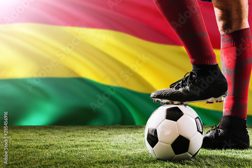 Close up legs of Bolivia football team player in red socks, shoes on soccer ball at the free kick or penalty spot playing on grass. © sezerozger