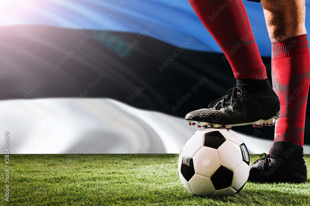 Close up legs of Estonia football team player in red socks, shoes on soccer ball at the free kick or penalty spot playing on grass.