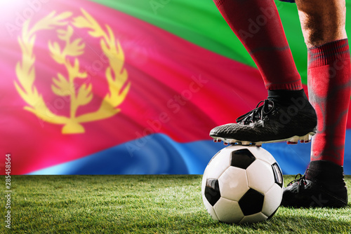 Close up legs of Eritrea football team player in red socks, shoes on soccer ball at the free kick or penalty spot playing on grass.