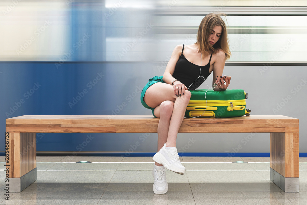 young lonely girl with suitcase waiting for train at station