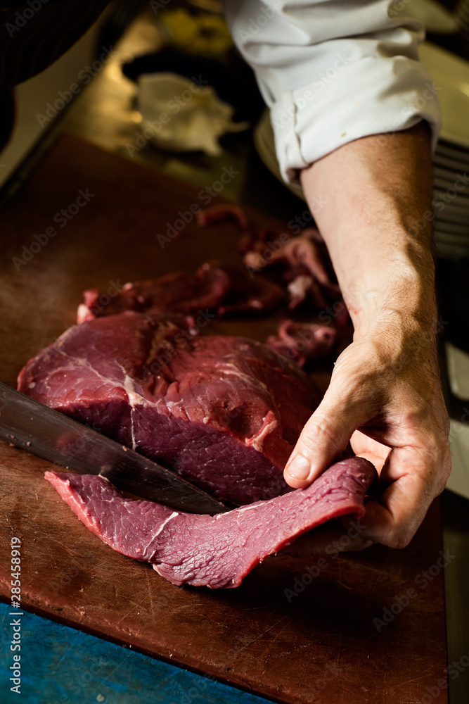 man cutting a piece of beef in a professional kitchen