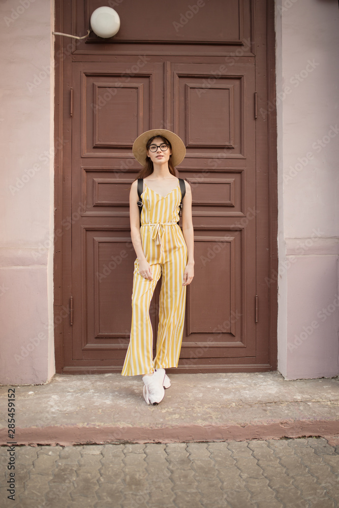 Fashionable young woman in a yellow suit stands near the door. Urban setting