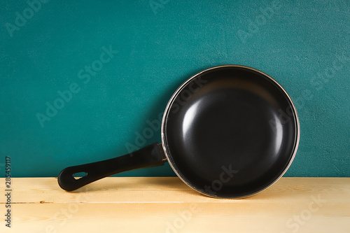 Black frying pan on a wooden shelf on teal background Tapéta, Fotótapéta