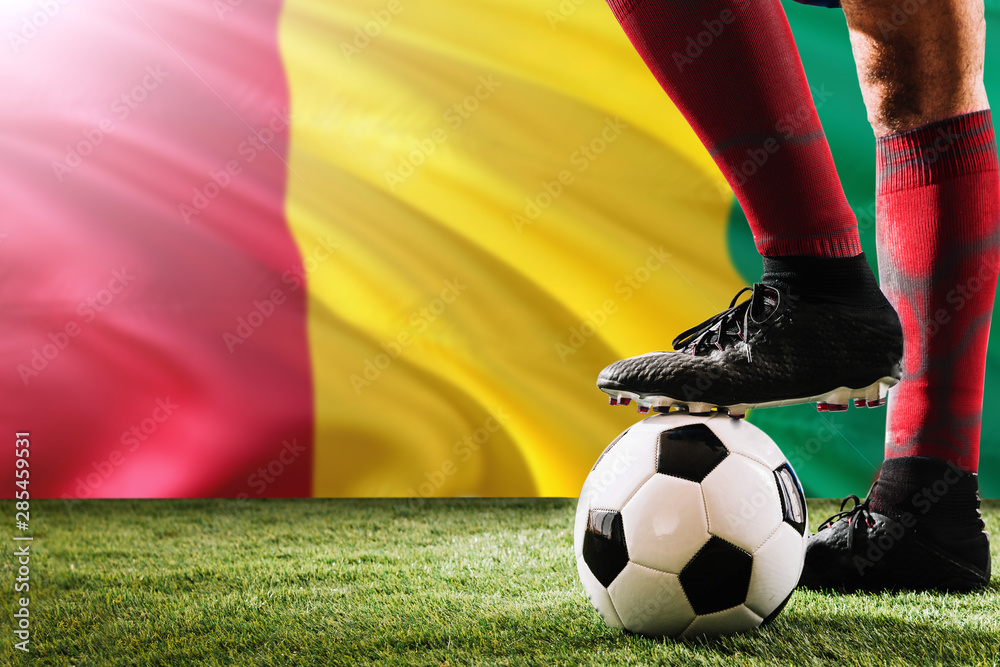 Close up legs of Guinea football team player in red socks, shoes on soccer ball at the free kick or penalty spot playing on grass.