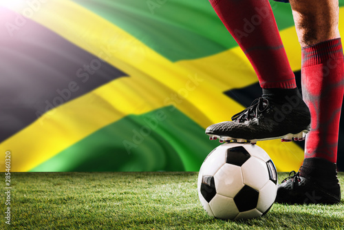 Close up legs of Jamaica football team player in red socks, shoes on soccer ball at the free kick or penalty spot playing on grass.