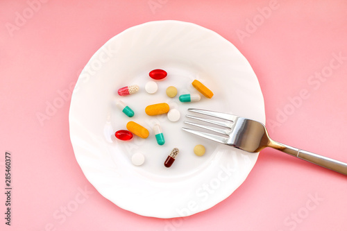 Many different weight loss pills and supplements as food on round white plate with fork. diet pills and supplements, prescription weight loss drugs, appetite suppressants for dieting concept photo