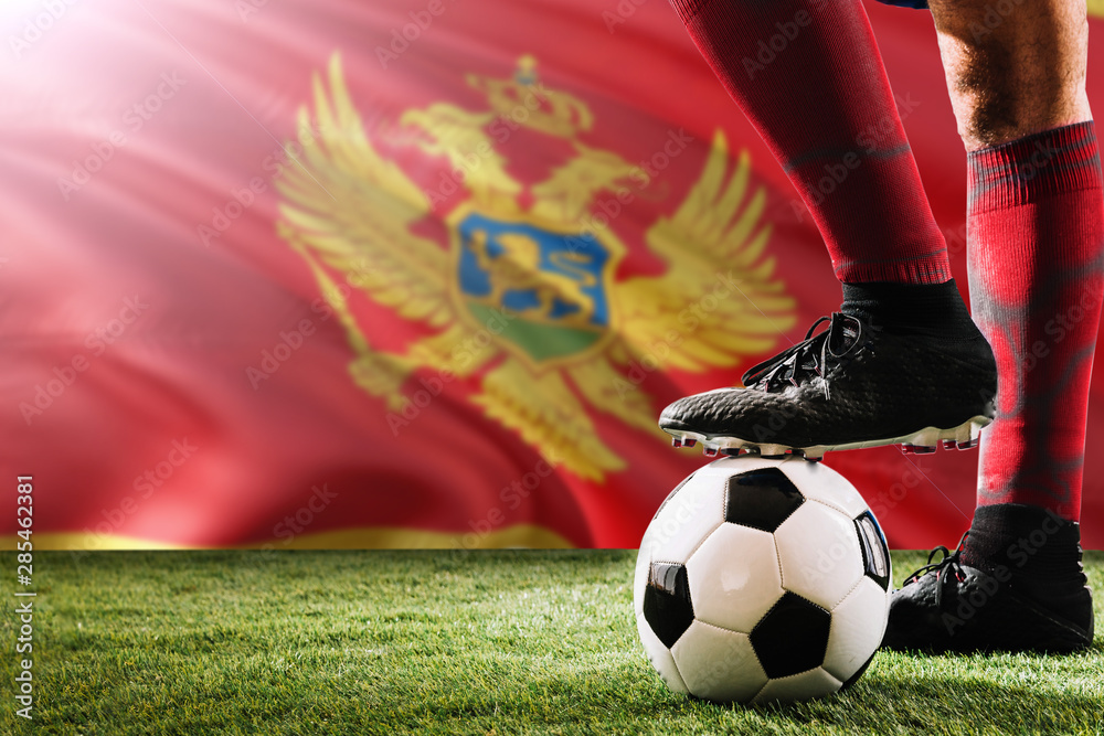 Close up legs of Montenegro football team player in red socks, shoes on soccer ball at the free kick or penalty spot playing on grass.