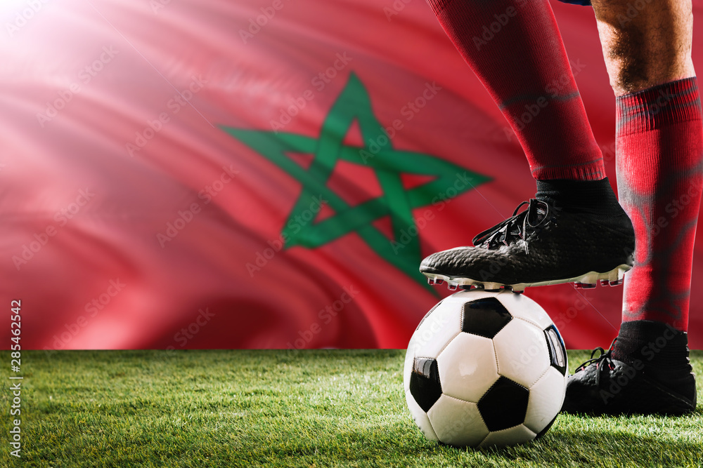 Close up legs of Morocco football team player in red socks, shoes on soccer ball at the free kick or penalty spot playing on grass.