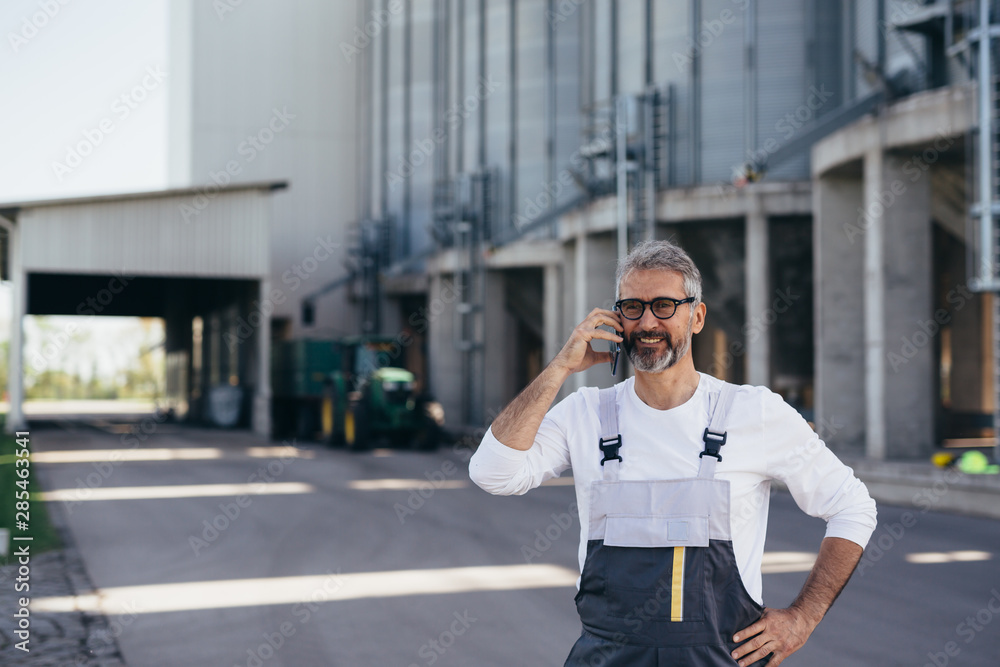 Fototapeta premium worker talking on mobile phone in front of grain silo outdoor