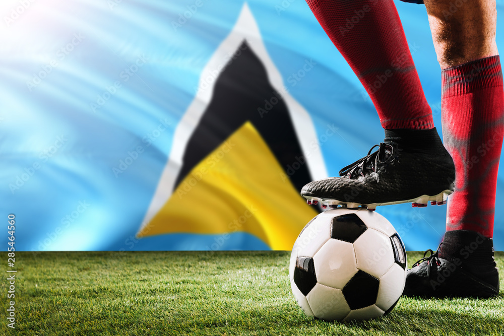 Close up legs of Saint Lucia football team player in red socks, shoes on soccer ball at the free kick or penalty spot playing on grass.