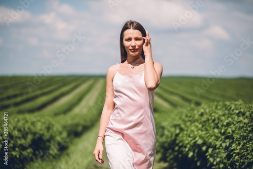 Beautiful girl in pink dress walking in the field of currants