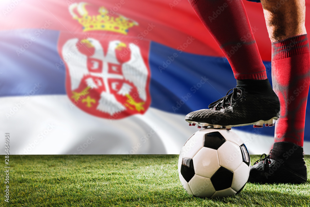 Close up legs of Serbia football team player in red socks, shoes on soccer ball at the free kick or penalty spot playing on grass.